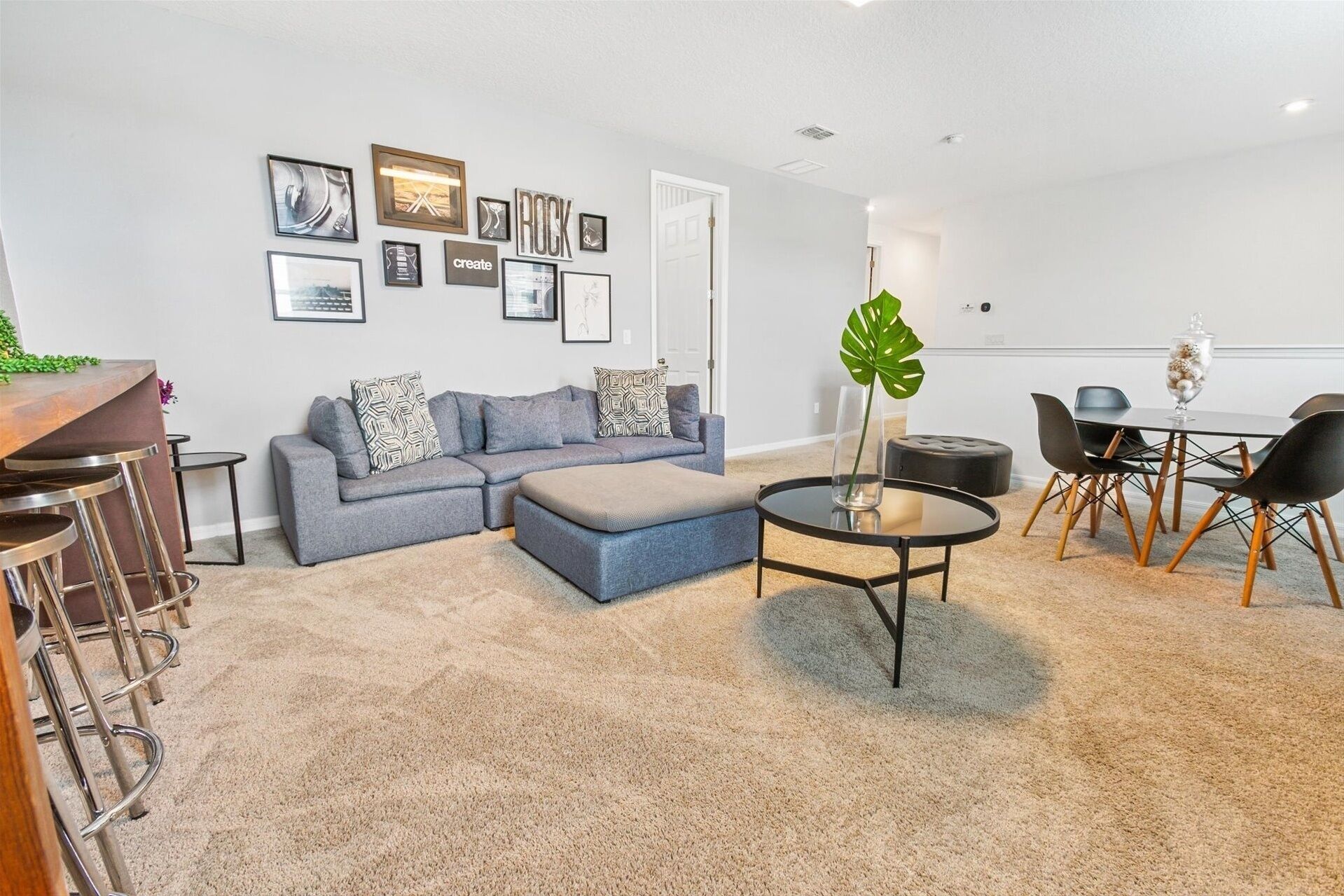 A modern living room with a grey sectional sofa, a round coffee table, and a dining area with a glass table and black chairs.