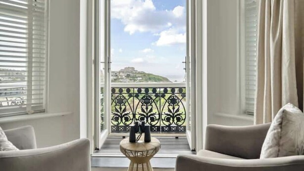 A room with a balcony, white walls, and a view of a hill and sea. - Beachfront Luxury Home with Hot Tub, 9 beds, Cinema room, Sleeps 2 to 16 (Newquay)
