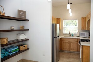 A compact kitchen with wooden cabinets, a stainless steel refrigerator, a microwave, and a window with blinds. - On Island -  New 2BR/2BA Condo with Central A/C, Convenient to Cruz Bay, Ocean Views (St John)