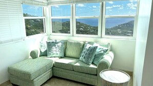 Ett hörnrum med en grön, modulbaserad soffa, flera fönster och utsikt över havet.