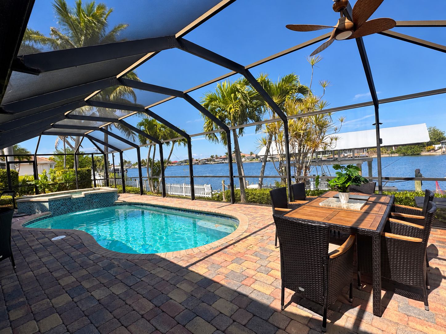 A covered outdoor swimming pool with a view of the water and palm trees.