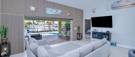 Una sala de estar moderna con un sofá gris, un televisor de pantalla plana y vistas a una zona de piscina al aire libre.