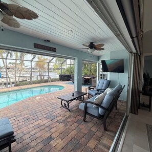 A covered outdoor area with a pool, lounge chairs, and a ceiling fan. - Waterfront Family Oasis- Pool, Spa, Kayaks & More! (Cape Coral)