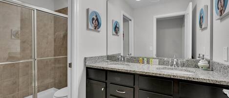 A modern bathroom with a glass shower enclosure, a white toilet, dark cabinets, and a granite countertop.