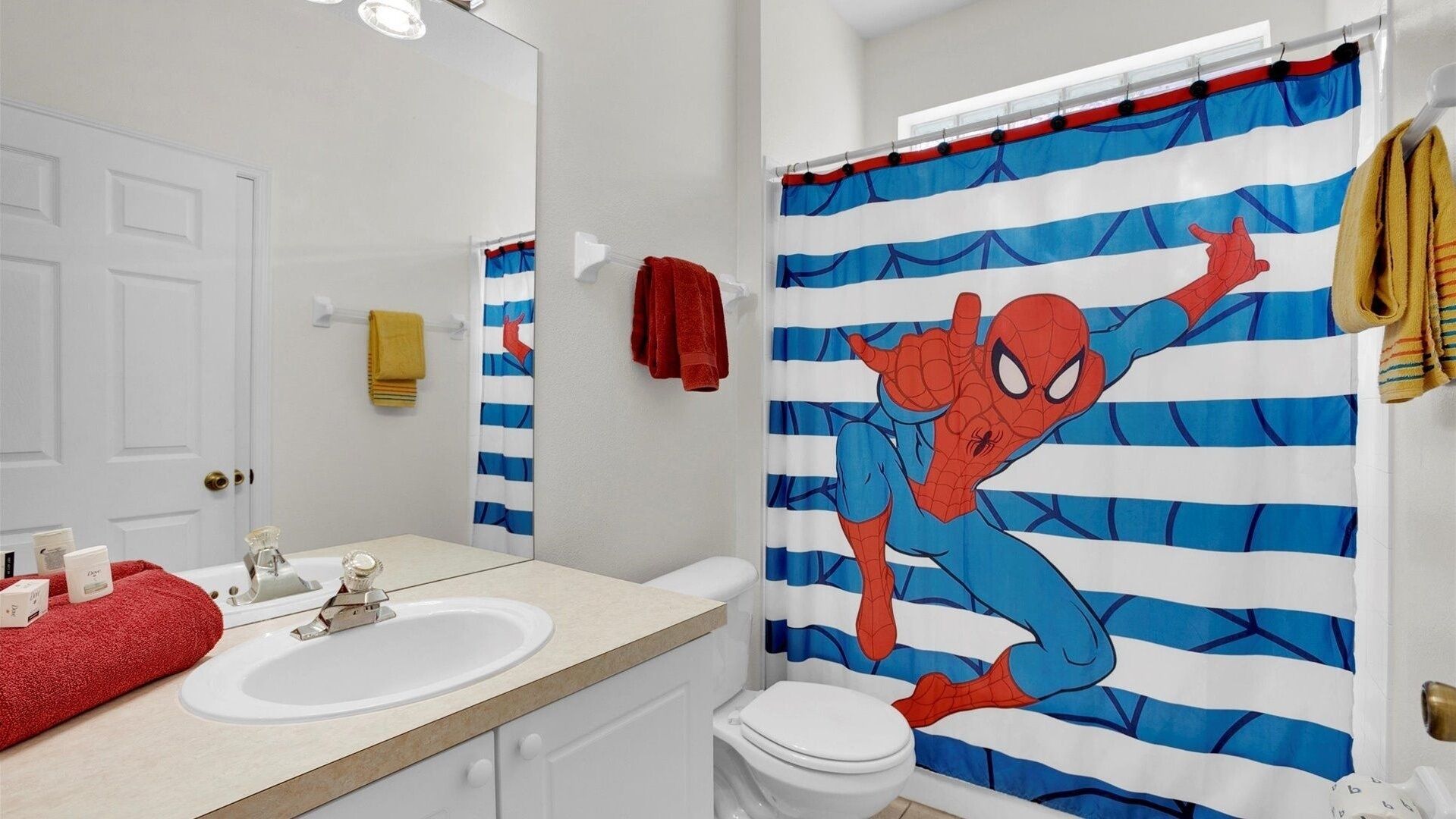 Une salle de bain avec un lavabo blanc, un miroir, des toilettes et un rideau de douche orné d’un motif Spider-Man.