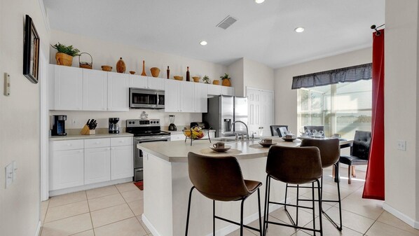 A modern kitchen with white cabinets, a central island with bar stools, a microwave, stove, and a refrigerator. - Windsor Palms Resort 4 Bedroom Private Pool Home 4 Home (Kissimmee)