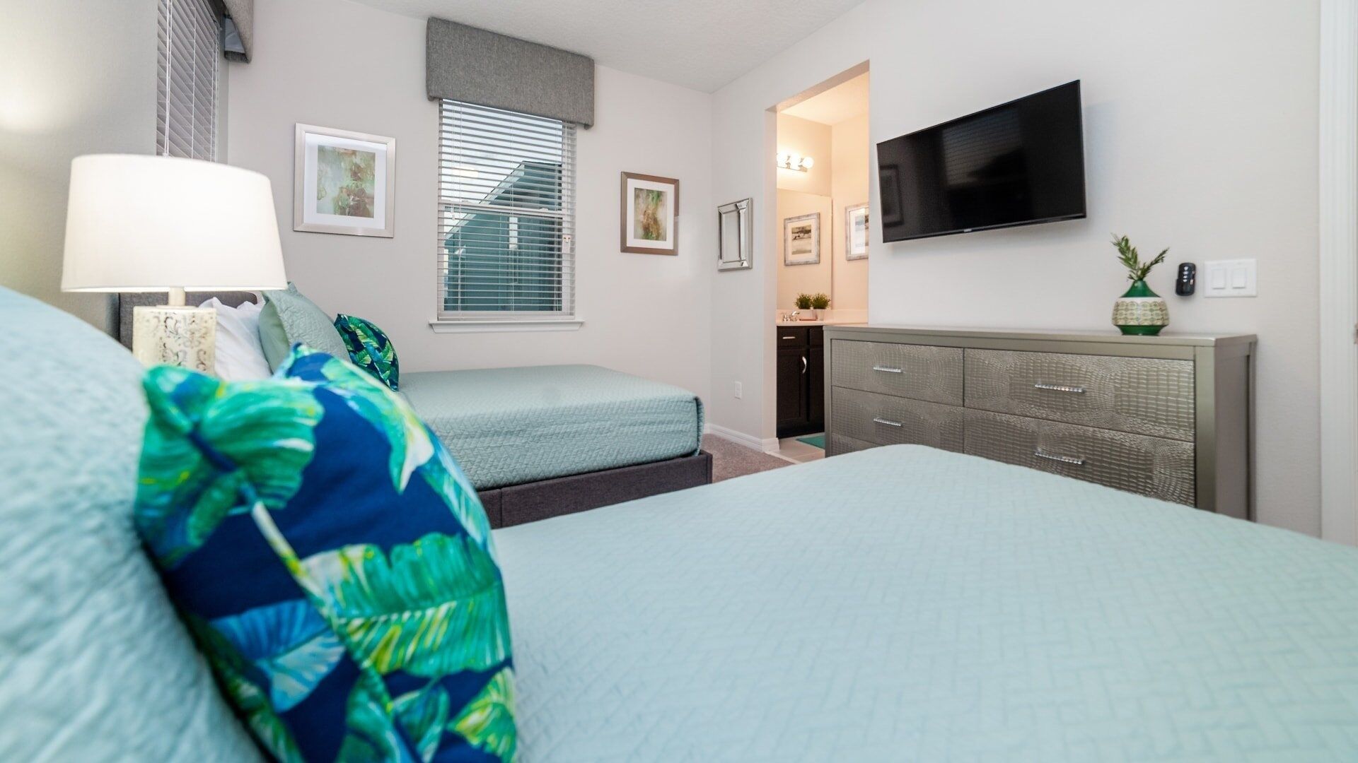 Un dormitorio con dos camas, televisor, cómoda y ventana con persianas.