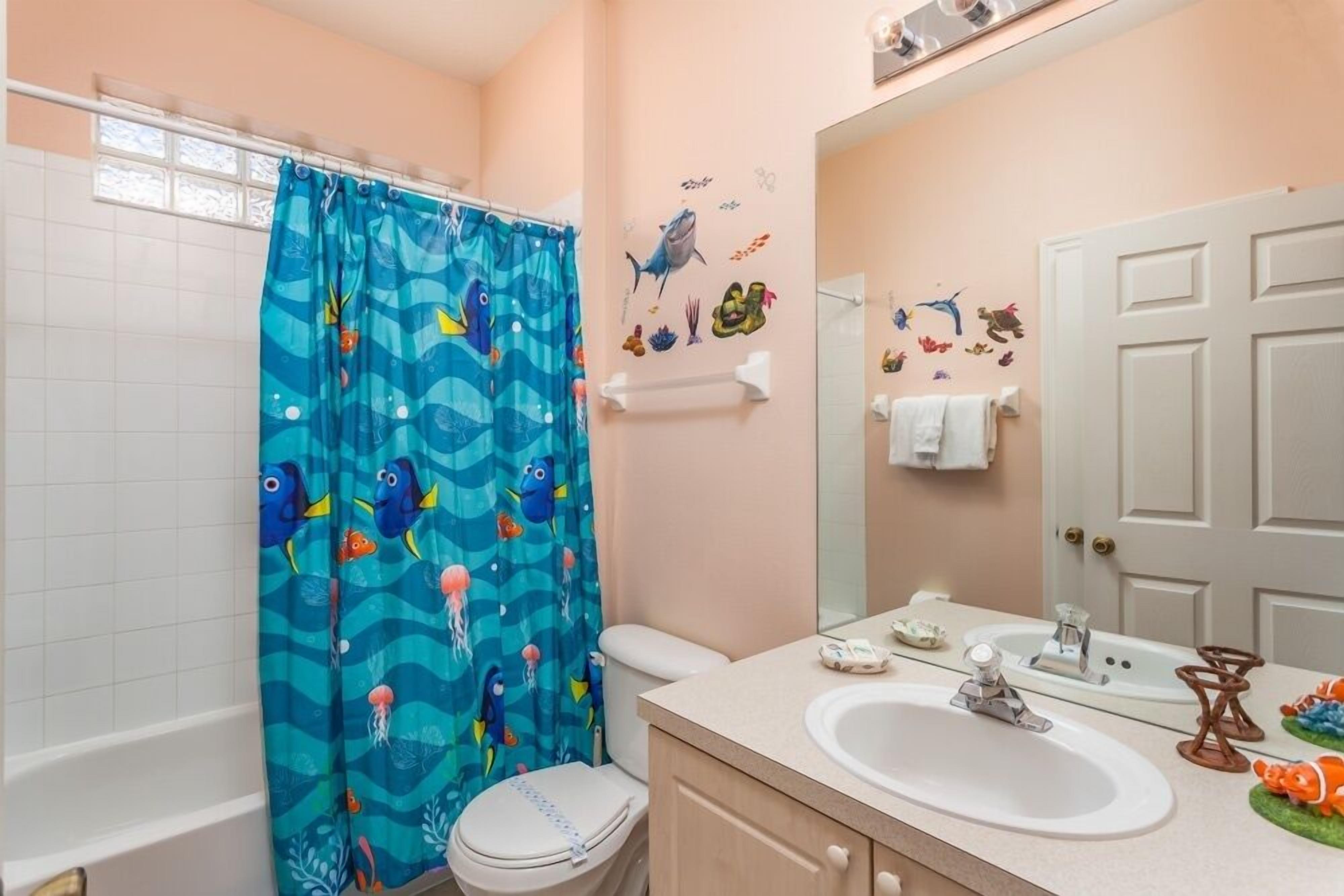 A bathroom with a shower curtain featuring a blue ocean theme, a white toilet, a sink with a mirror, and wall decorations of sea creatures.