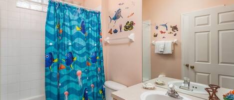 A bathroom with a shower curtain featuring a blue ocean theme, a white toilet, a sink with a mirror, and wall decorations of sea creatures.