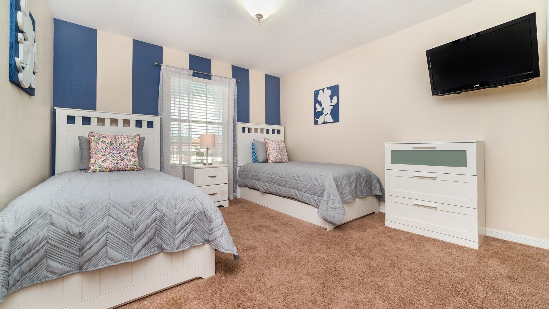 A bedroom with two beds, a dresser, a TV, and a window with curtains.