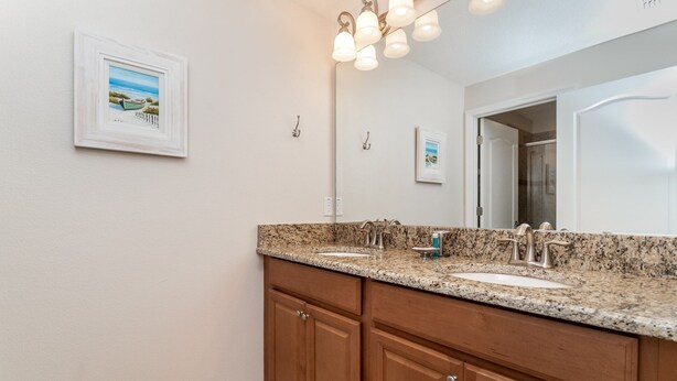 A bathroom with a granite countertop, double sink, wooden cabinets, and a large mirror with a beach scene picture. - Paradise Palms Resort 4 Bedroom Private Pool Townhome 4 Townhouse (Kissimmee)