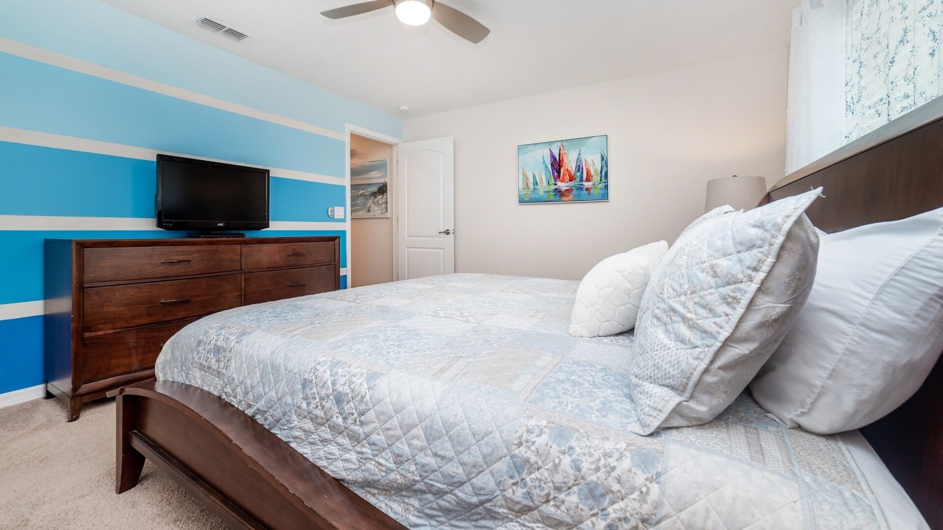 A bedroom with a bed, a dresser, a television, and a painting on the wall.