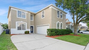 Une maison à deux étages avec un garage, une allée et une pelouse bien entretenue.