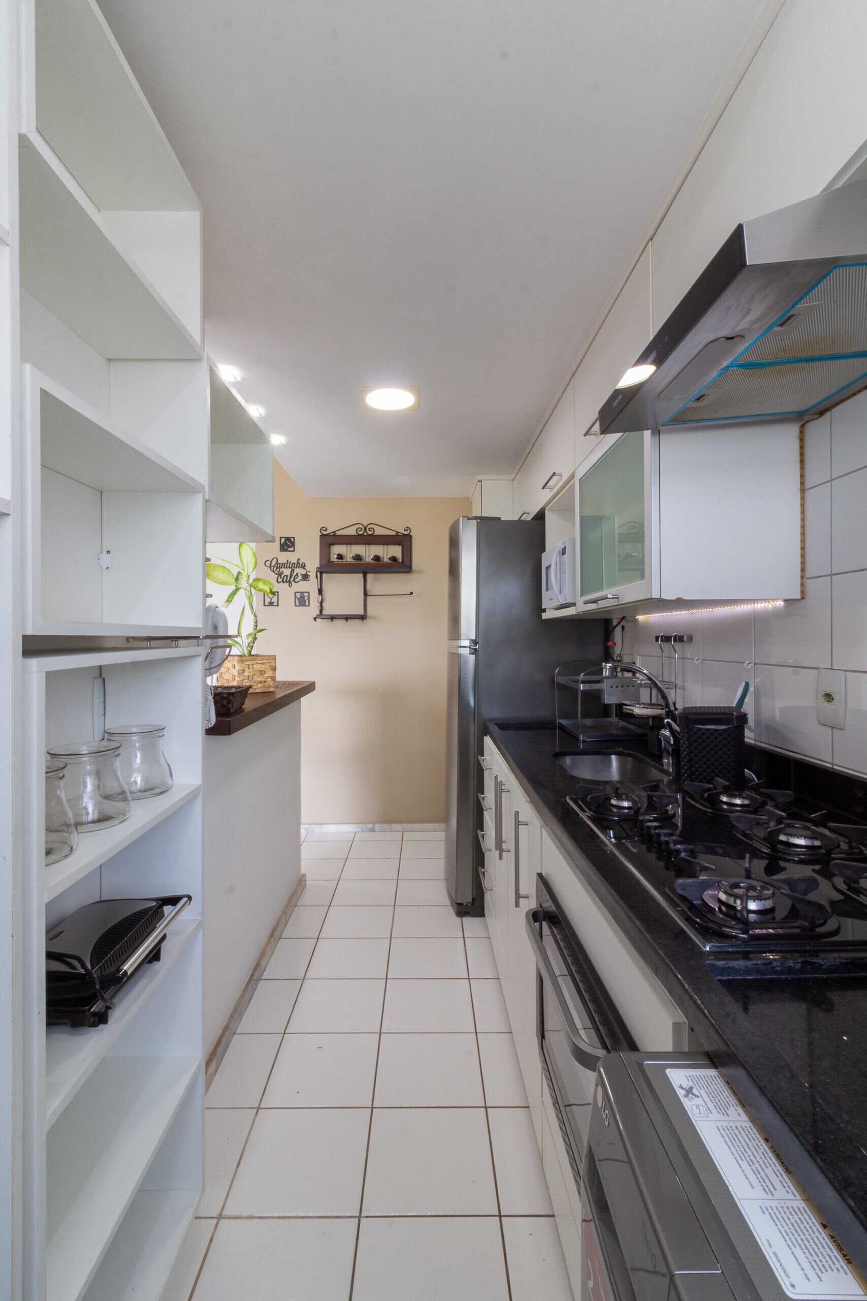 A kitchen with white cabinets, a black stove, and a refrigerator. There are shelves with jars and a potted plant.