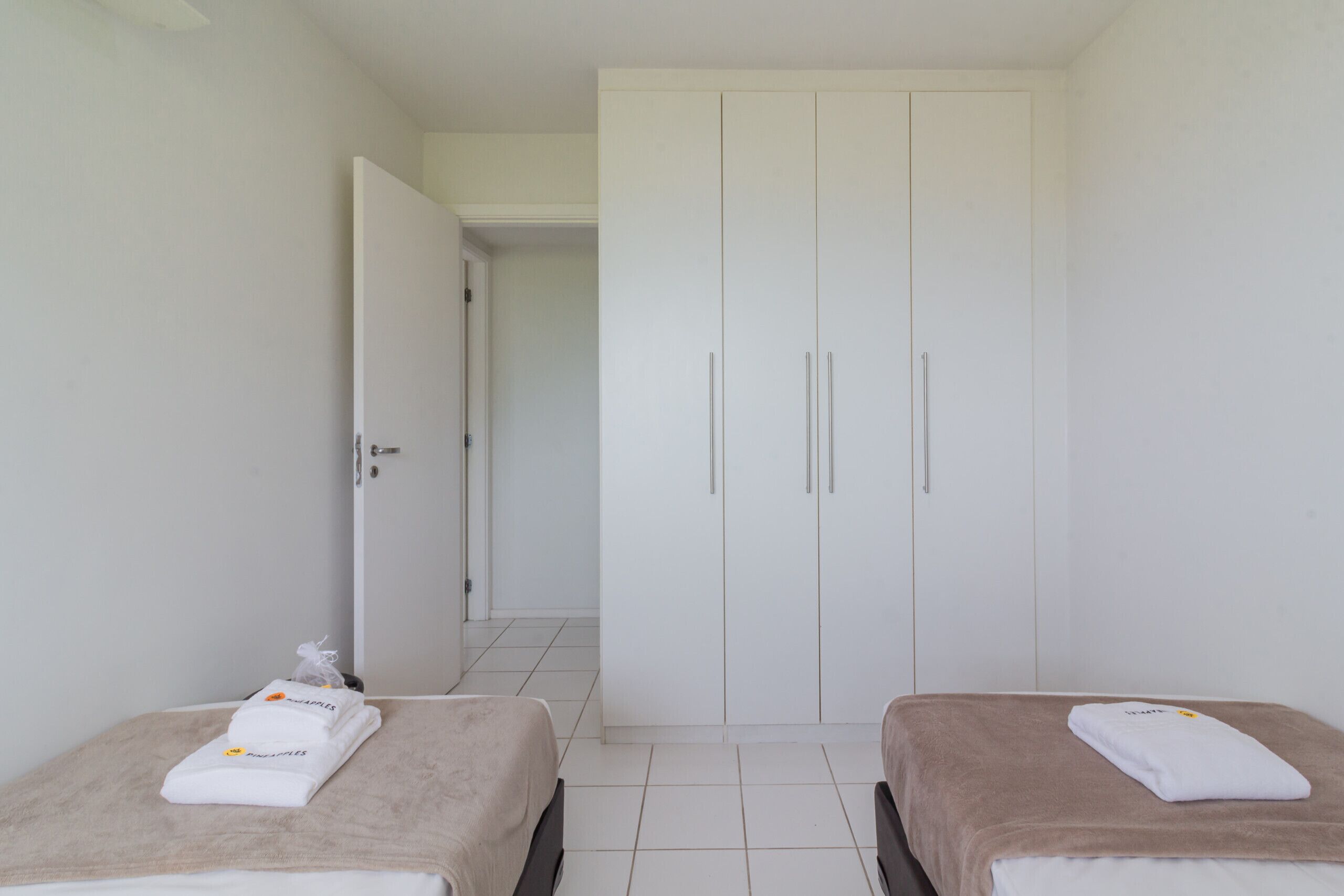 A hotel room with two beds, a wardrobe, and a bathroom visible in the background.