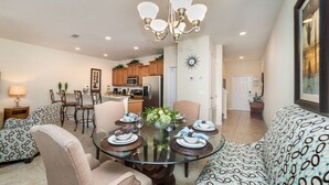 A modern living room with a glass dining table, patterned sofas, and a kitchen in the background. - Paradise Palms Resort 4 Bedroom Private Pool Townhome 4 Townhouse (Kissimmee)