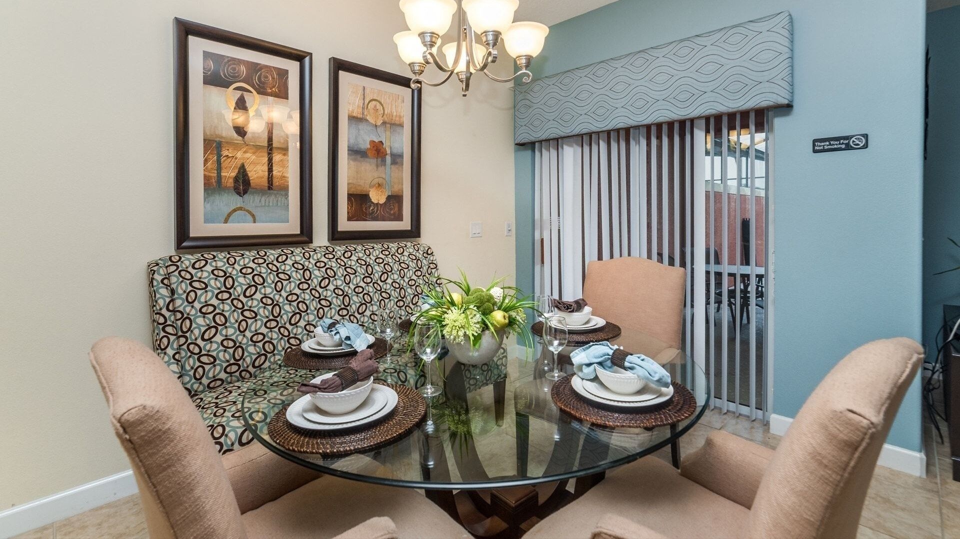 A dining area with a glass table, two chairs, a patterned sofa, and a chandelier.