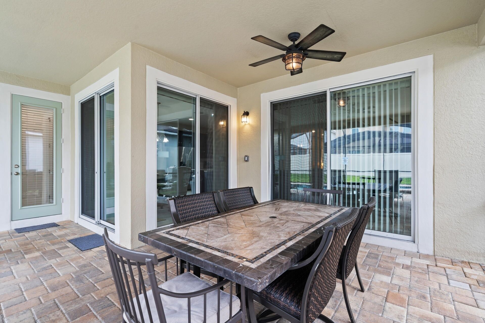 An outdoor patio with a table and chairs, a ceiling fan, and large sliding glass doors.