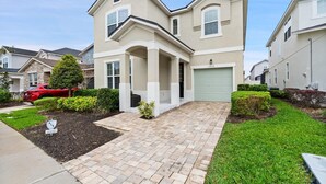 A two-story residential building with a garage, a driveway, and well-maintained landscaping. - Solara Resort 6 Bedroom Private Pool Home 6 Home (Kissimmee)