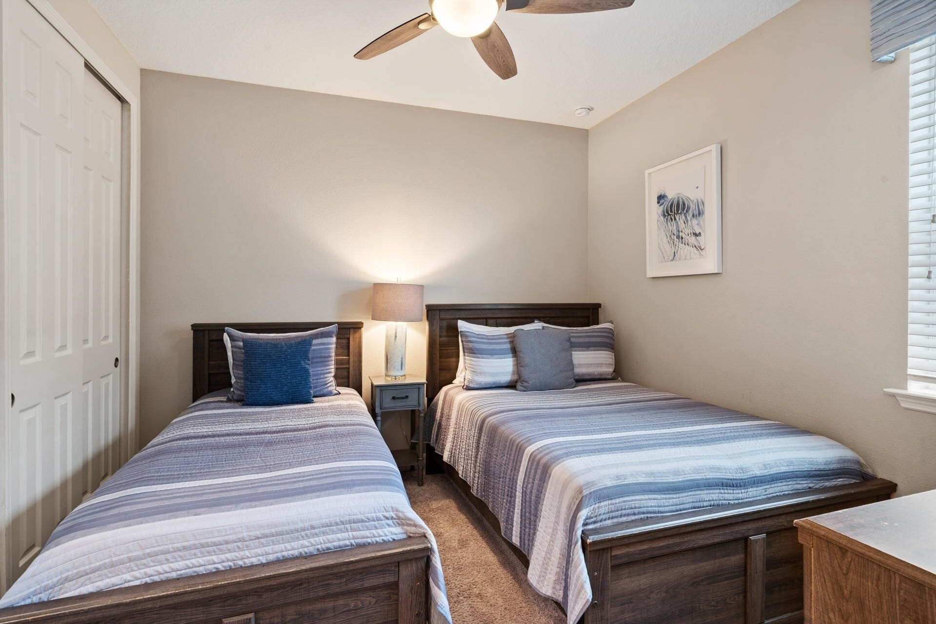 A bedroom with two beds, a ceiling fan, a bedside lamp, and a framed picture on the wall.