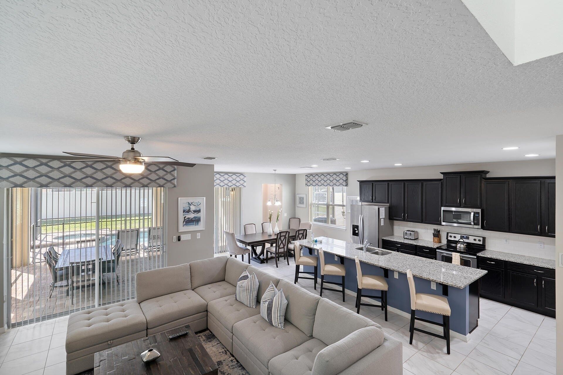 A modern kitchen with dark cabinets, a central island, and a dining area with a sofa and chairs.