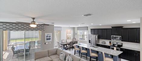 A modern kitchen with dark cabinets, a central island, and a dining area with a sofa and chairs.