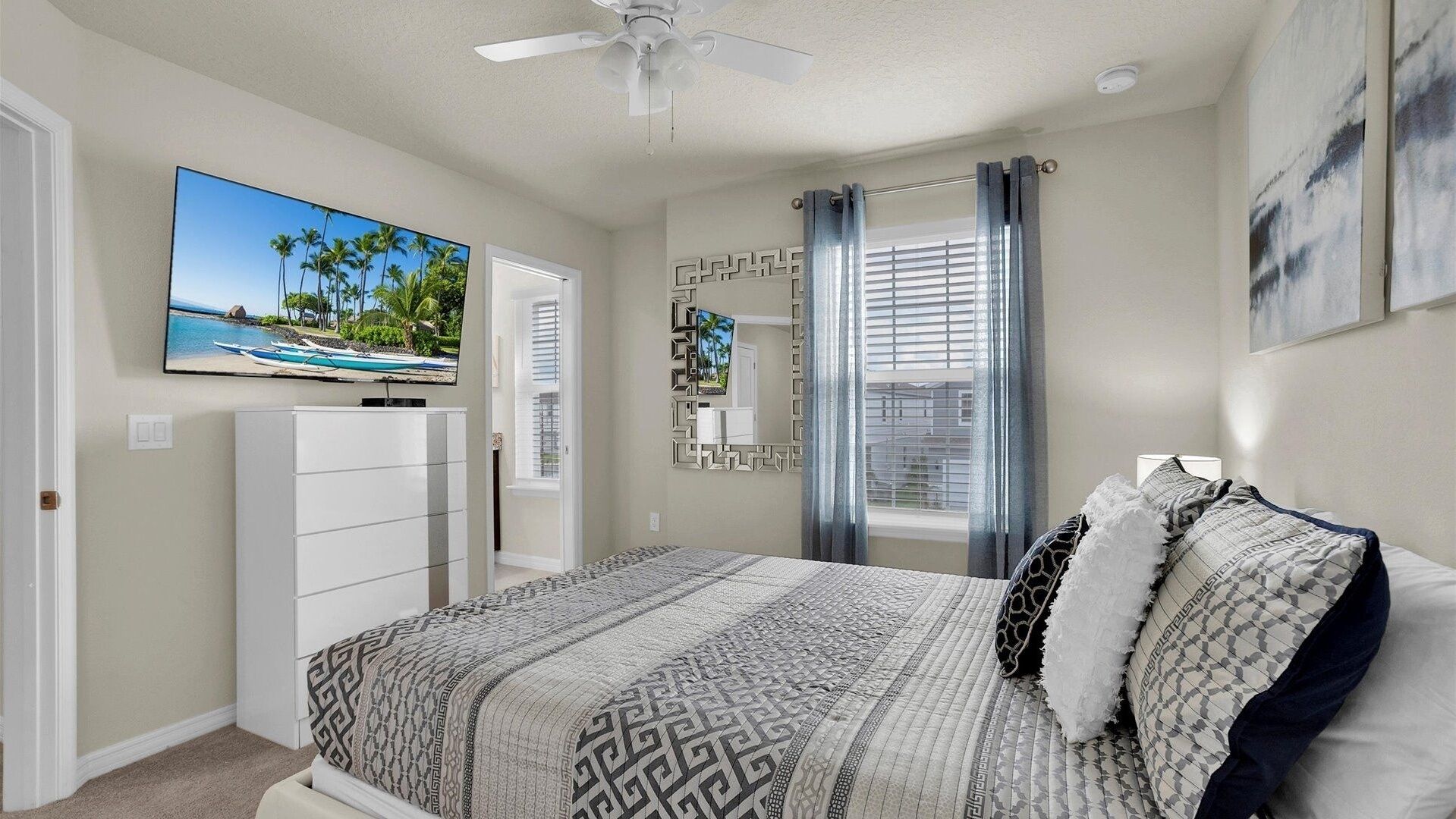 A bedroom with a bed, a TV, a dresser, a ceiling fan, and a window with curtains.