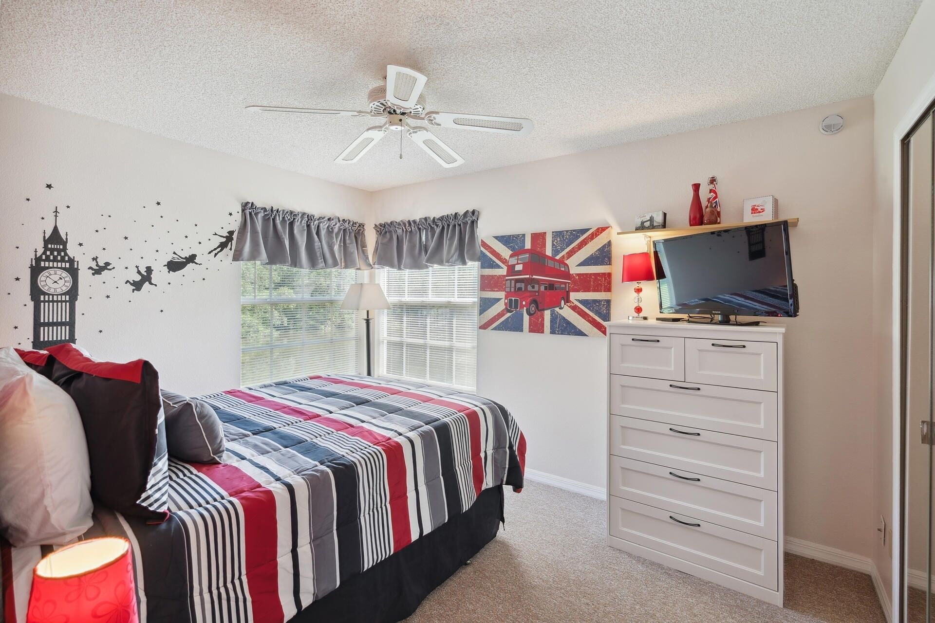 A bedroom with a bed, a dresser, a TV, and a ceiling fan.