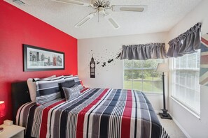 A bedroom with a red wall, a bed with striped bedding, a framed picture, a wall decal, and a window with curtains. - Sweetwater Club 3 Bedroom Condo 7 miles to Disney 3 Condo (Kissimmee)