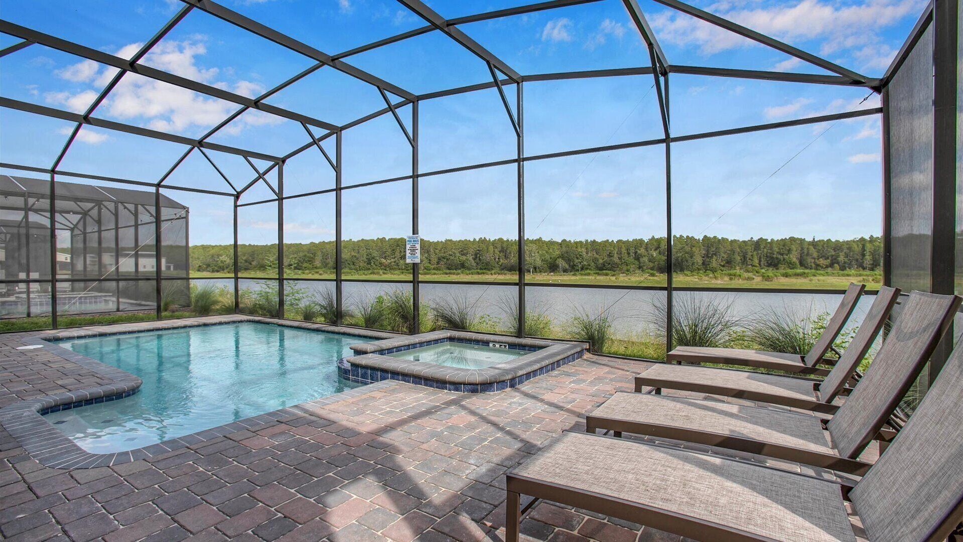 Un área de piscina con un jacuzzi, sillas de descanso y vistas a un lago y un bosque.