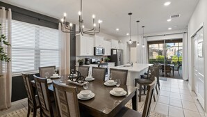 A modern kitchen with white cabinets, a stainless steel refrigerator, and a dining area with a dark wooden table and chairs. - Solterra Resort 5 bedroom Private Pool/Spa Home 5 Home (Davenport)