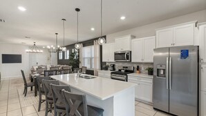 A modern kitchen with white cabinets, stainless steel appliances, and a central island with bar stools. - Solterra Resort 5 bedroom Private Pool/Spa Home 5 Home (Davenport)