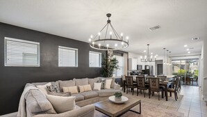 A modern living room with a sectional sofa, a coffee table, and a dining area with chairs and a table. - Solterra Resort 5 bedroom Private Pool/Spa Home 5 Home (Davenport)