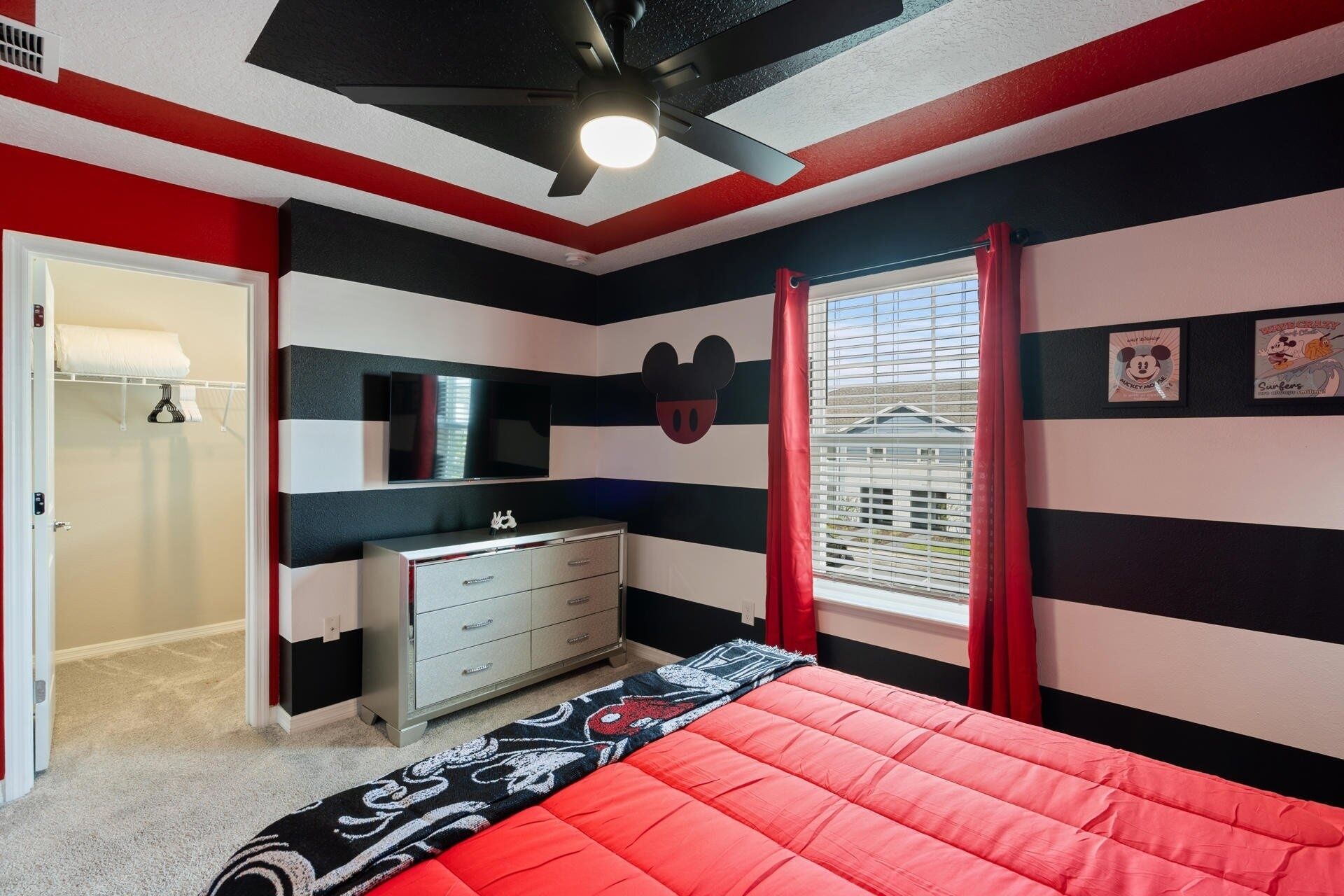 A bedroom with a bed, dresser, and Mickey Mouse wall decoration.