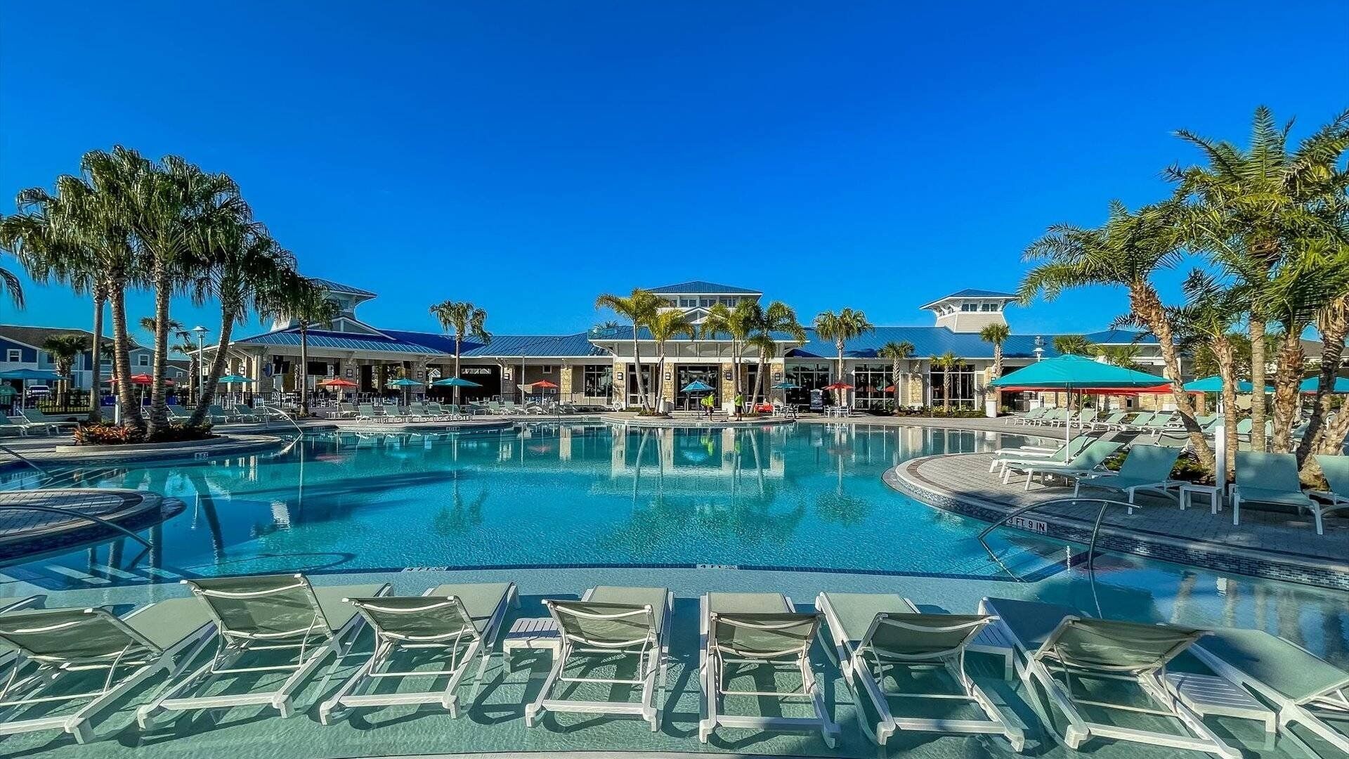 Een zwembad van een resort met helderblauw water, omgeven door palmbomen en ligstoelen.