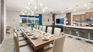 A modern kitchen with a large island, bar stools, and a dining area with a long table set for six. - Windsor Island Resort 10 Bedroom Themed Private Home with Pool+Spa & Resort Amenity Access 10 Home (Davenport)