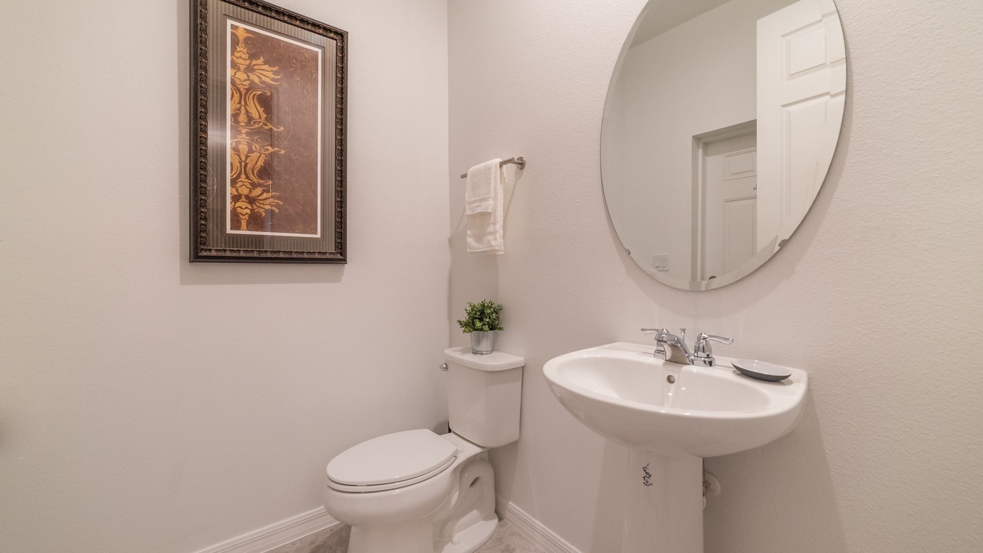 A bathroom with a toilet, sink, and a framed picture on the wall.