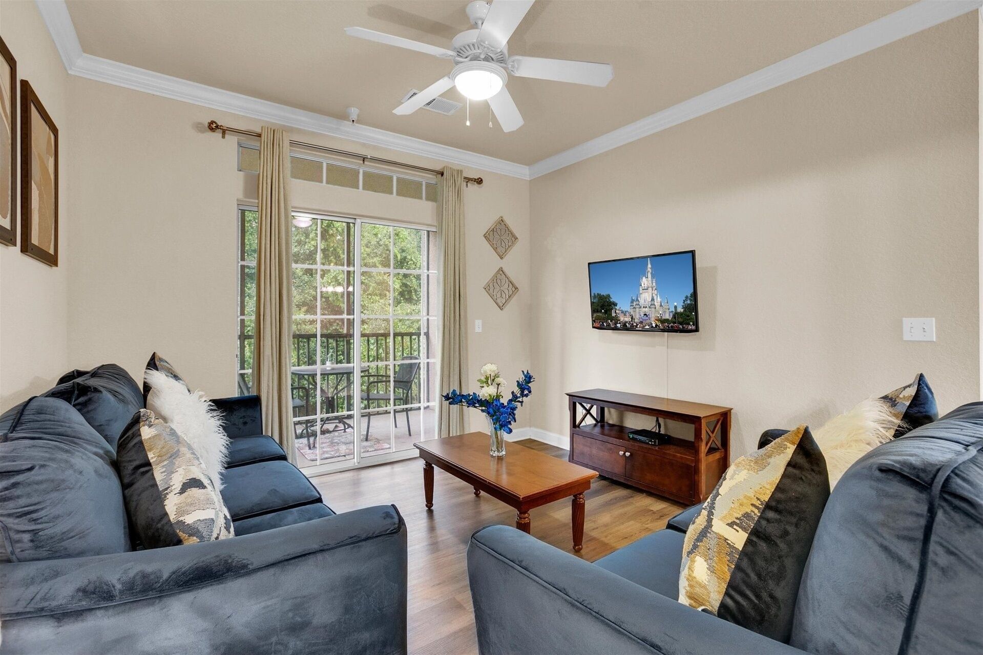 A living room with a ceiling fan, a large window with curtains, a wooden coffee table, and a television on the wall.