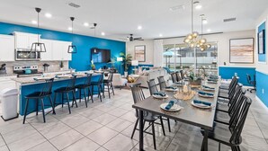 A modern kitchen with white cabinets, a blue accent wall, and a dining area with a large table set for six. - Windsor Island Resort 10 Bedroom Themed Private Home with Pool+Spa & Resort Amenity Access 10 Home (Davenport)