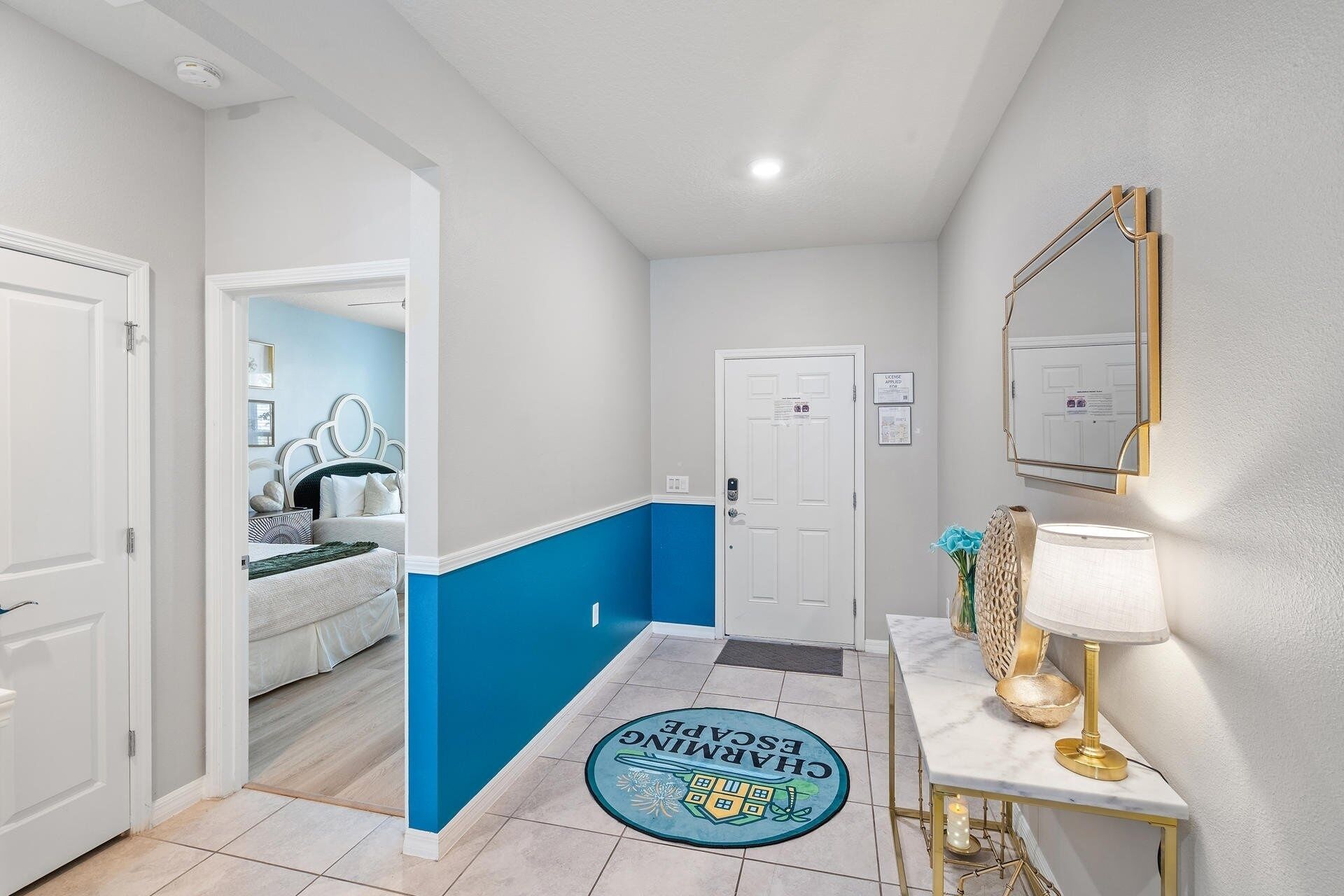 A hallway with a blue accent wall, a white door, a marble console table with a lamp, and a doormat with a logo.