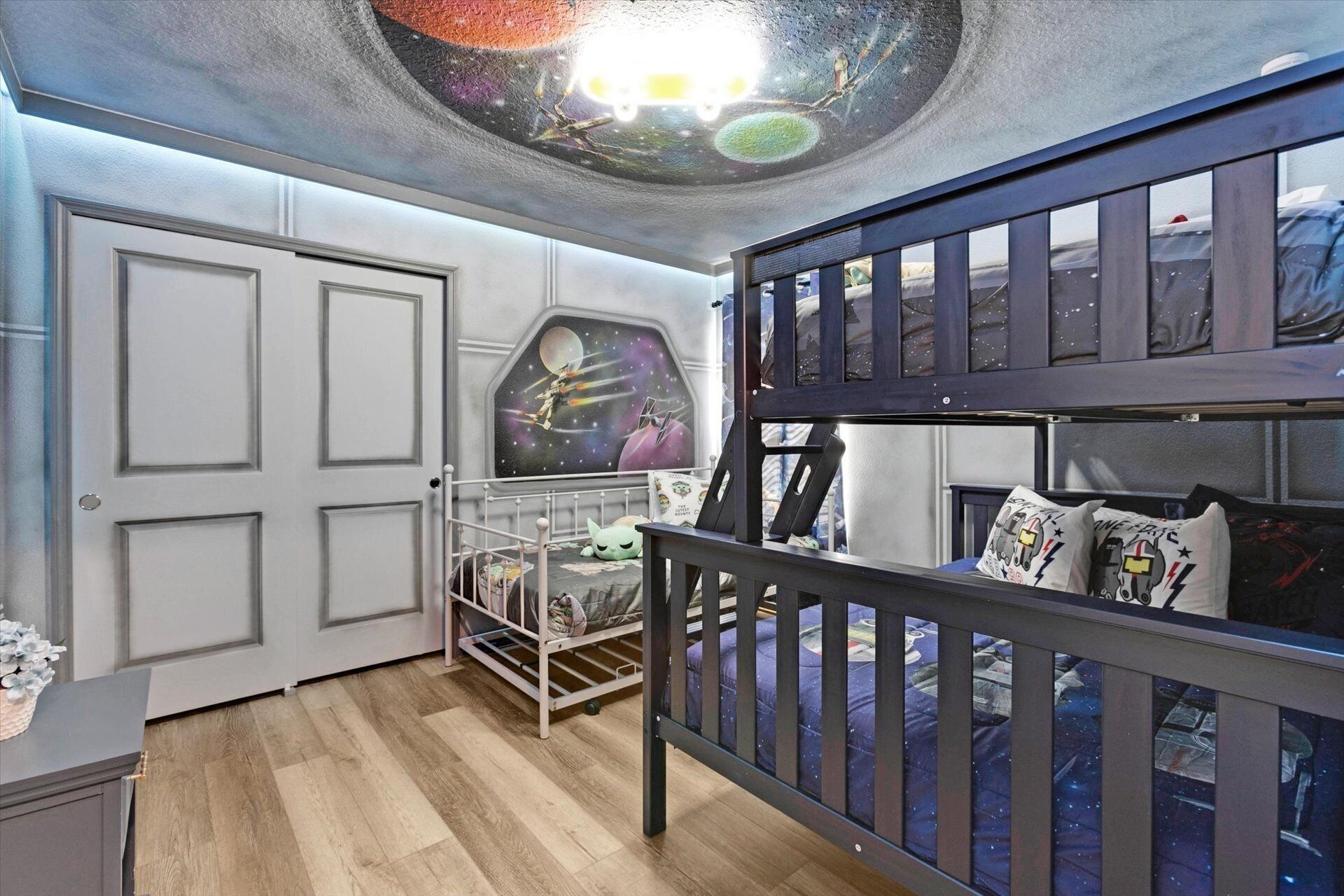 Habitación de literas infantil con techo decorado con motivos galácticos, una puerta y una ventana que da a un paisaje nevado.