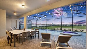 A spacious indoor area with a pool, a dining table with chairs, and a view of fireworks. - New 10 Br/19 Beds Pool+spa Disney Fireworks View 10 Bedroom Home (Davenport)