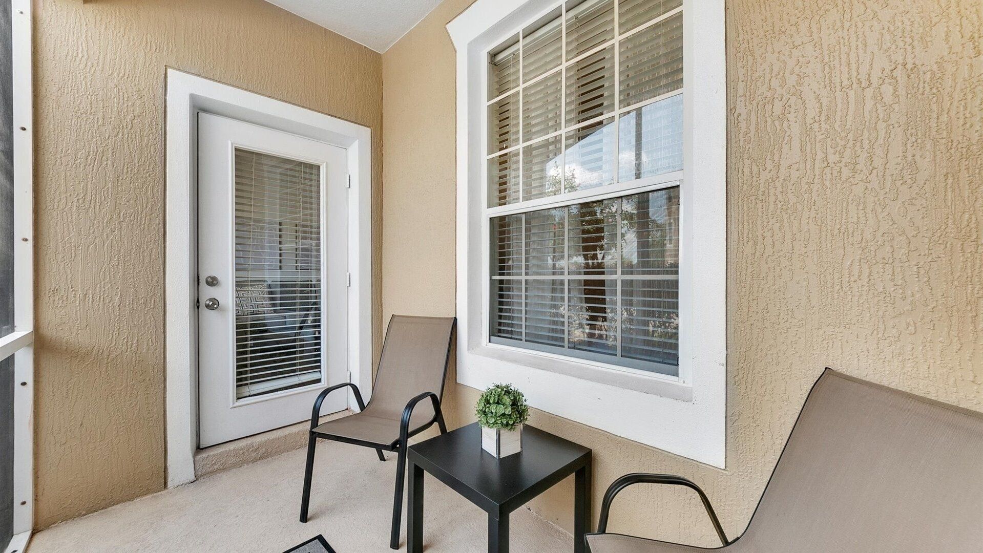 A small, enclosed balcony with a door, a window, and two chairs.