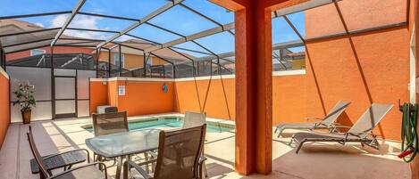 A covered outdoor area with a pool, lounge chairs, and a table with chairs.