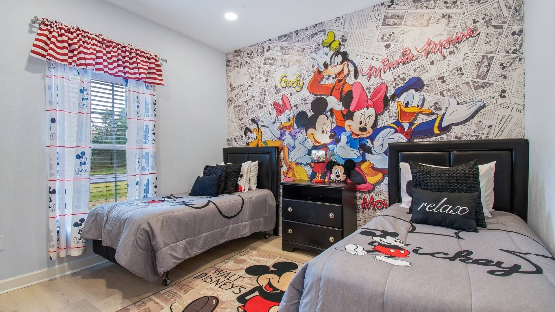 Habitació amb dos llits, un mural amb dibuixos de Mickey Mouse i roba de llit amb temàtica de Mickey Mouse.