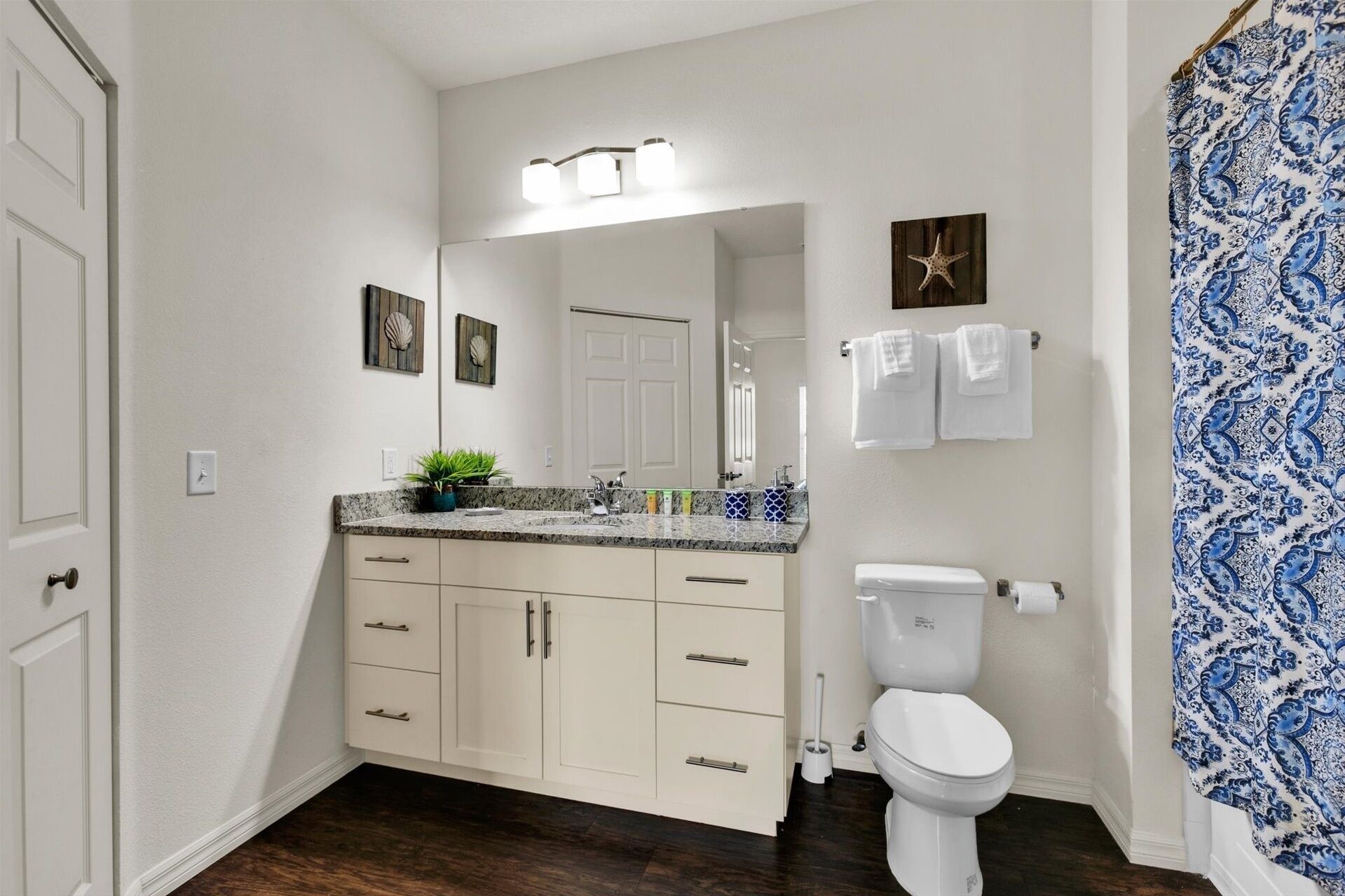 A bathroom with a white toilet, a sink with a marble countertop, and a shower curtain with a blue pattern.
