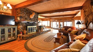 A cozy living room with a stone fireplace, leather sofa, and a television. - Rare 4-Home Compound on Sebago Lake Peninsula With 360° Views (Raymond)