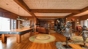 A spacious room with a wooden floor, a pool table, a bookshelf, and a statue of a child. - Rare 4-Home Compound on Sebago Lake Peninsula With 360° Views (Raymond)