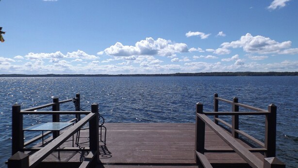 A wooden pier extending into a calm body of water with a clear sky above. - Rare 4-Home Compound on Sebago Lake Peninsula With 360° Views (Raymond)