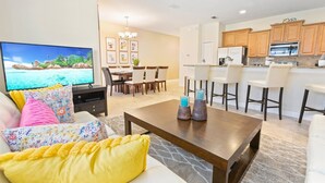 A living room with a TV, sofa, coffee table, and a dining area with chairs and a table. - Paradise Palms Resort 4 Bedroom Private Pool Townhome 4 Townhouse (Kissimmee)